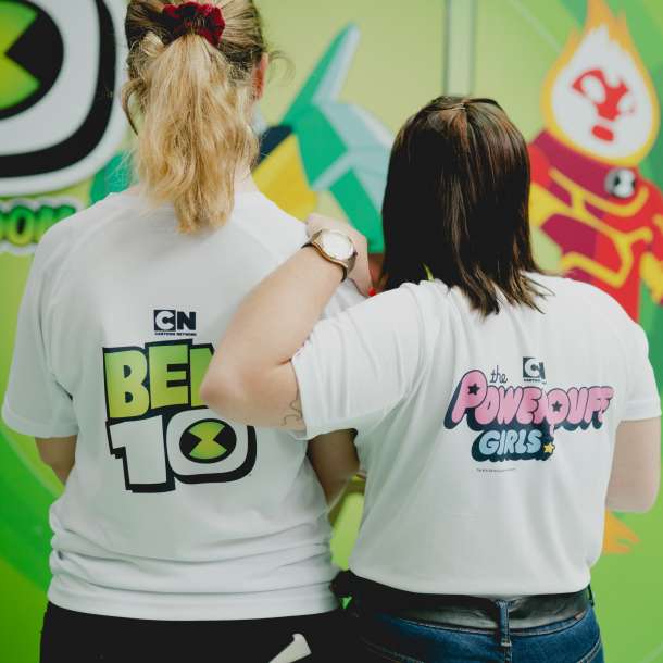 Promotores de costas a mostrar o vestuário de identificação do evento referentes às séries "Ben10" e "The Power Puff Girls"